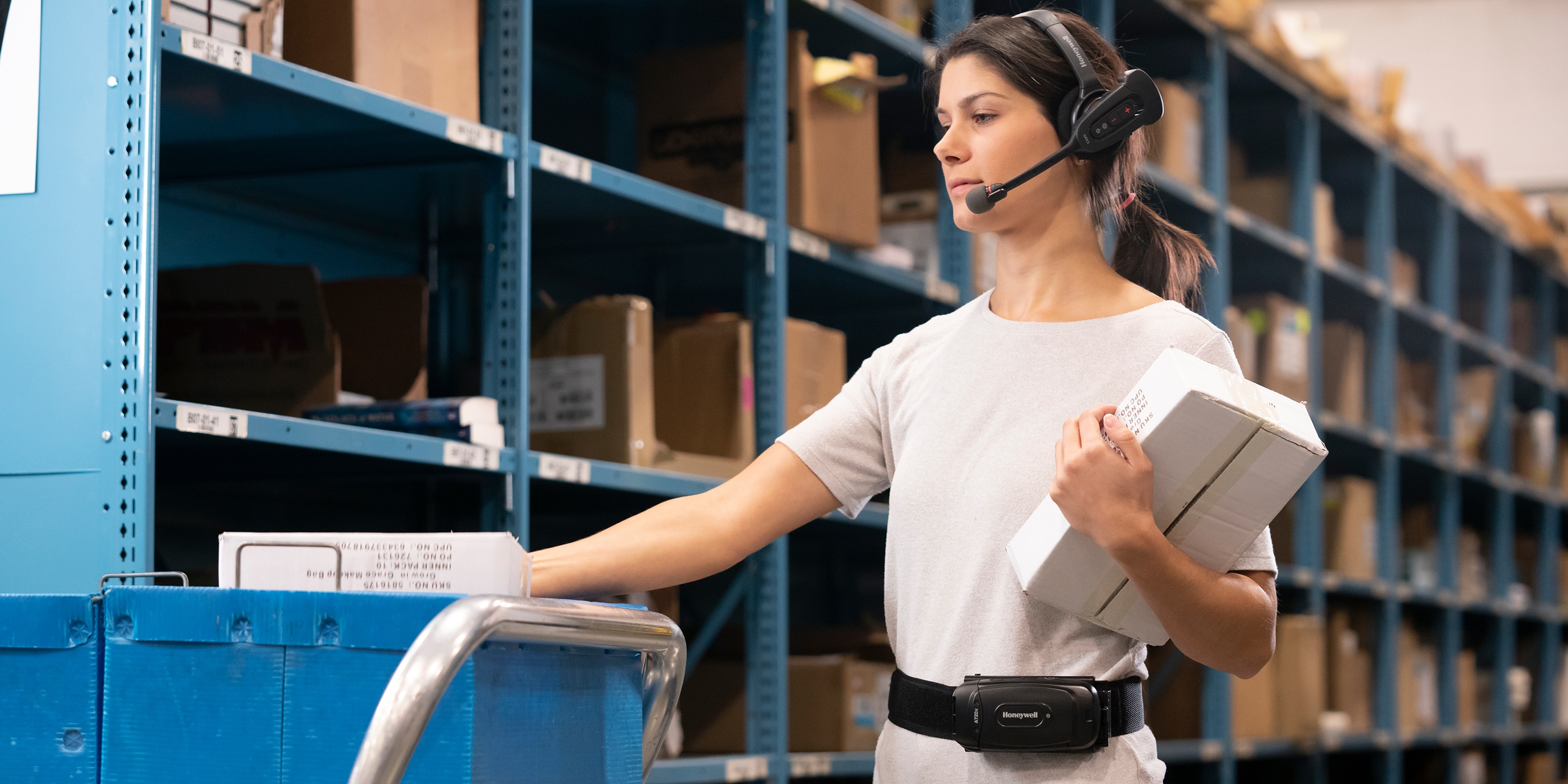 Warehouse worker using Honeywell voice-directed headset and belt device for hands-free picking operations